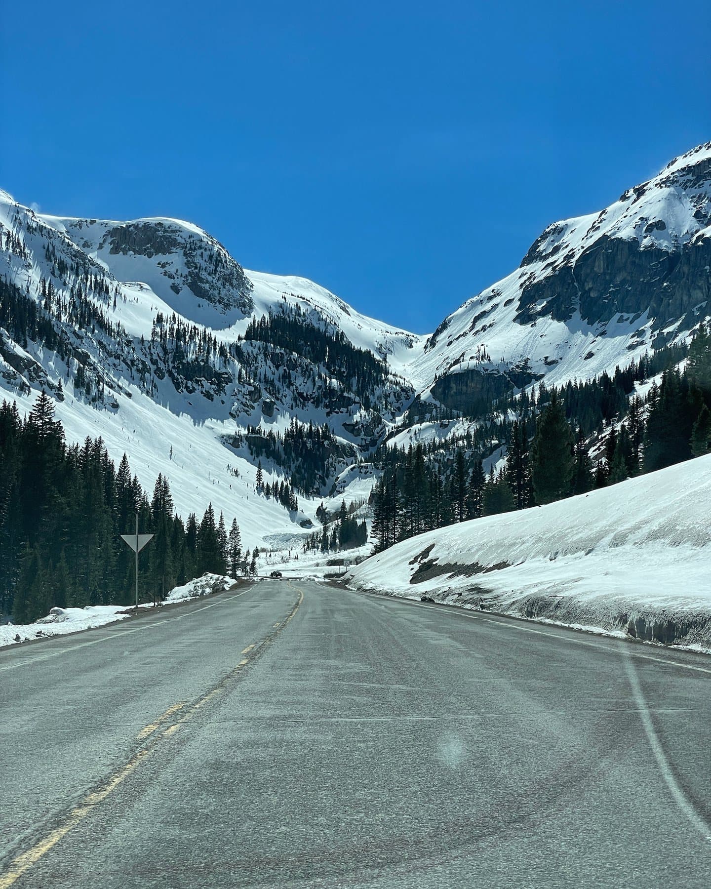 A snow-lined mountain road stretching toward a high alpine pass.