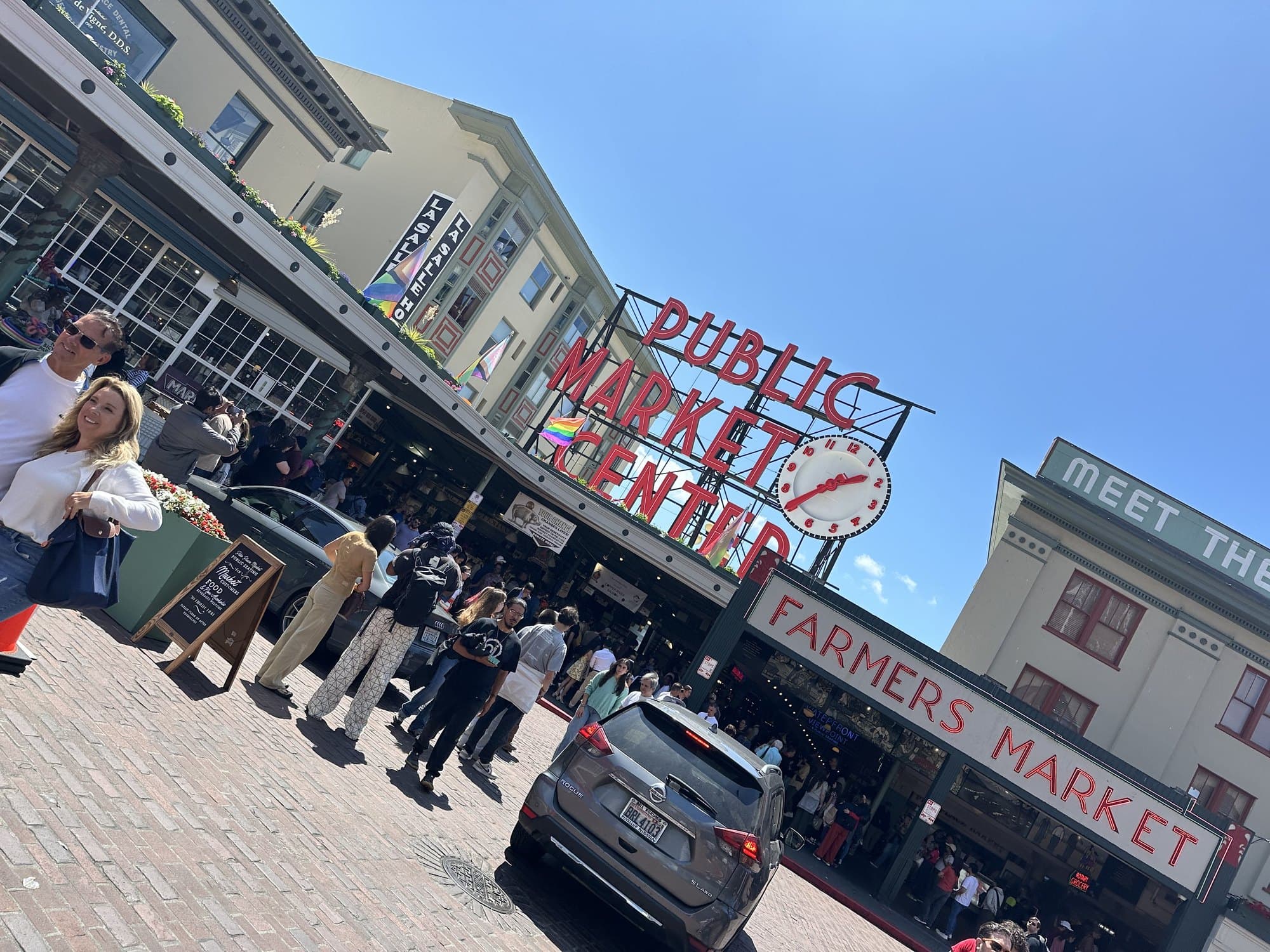 The red Public Market Center sign above a crowd of shoppers on a sunny day.
