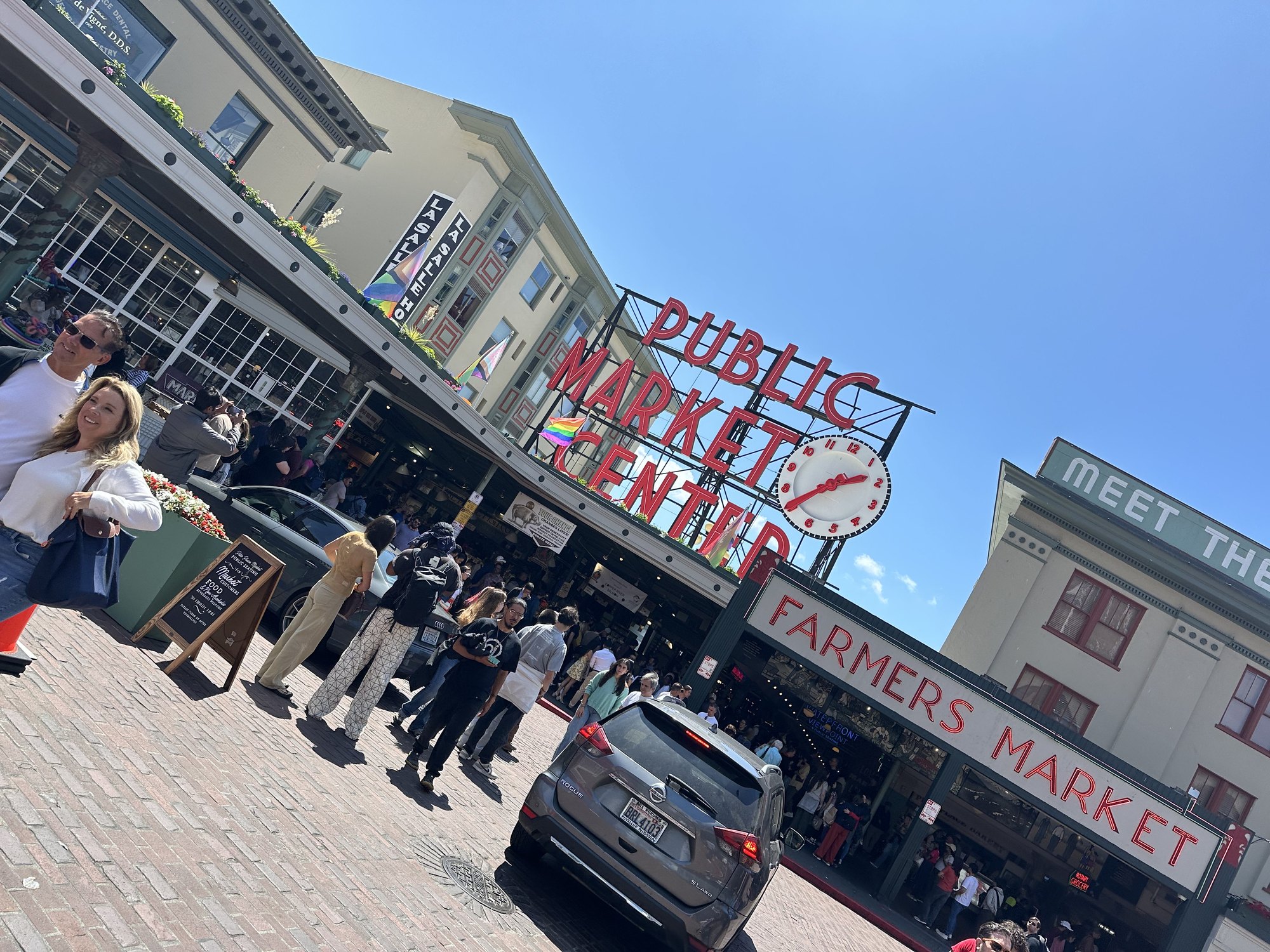 The red Public Market Center sign above a busy market street on a clear day.
